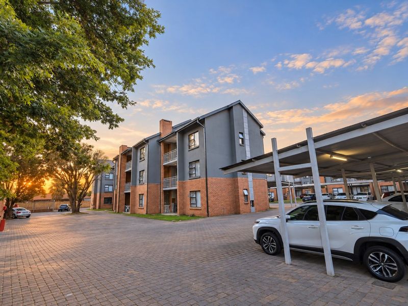 Exterior view of a modern apartment complex featuring brick and rendered facades, paved parking areas, and covered carports at sunset.