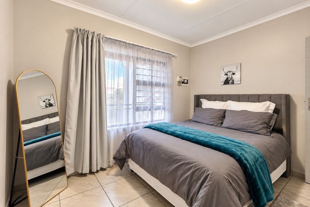 A well-maintained bedroom featuring neutral wall tones, tiled flooring, and a window fitted with a security gate and curtains.
