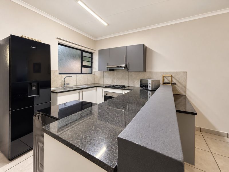 Modern kitchen featuring granite countertops, a breakfast bar, built-in oven, gas hob, extractor fan, and ample cabinetry with a tiled backsplash.