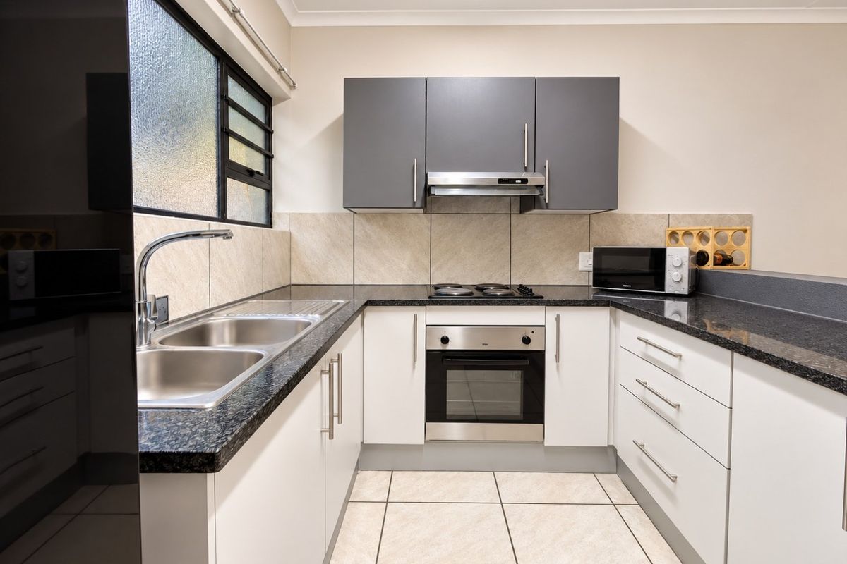 Modern kitchen featuring granite countertops, built-in oven, electric hob, extractor fan, and ample storage cabinetry with a double bowl stainless steel sink.