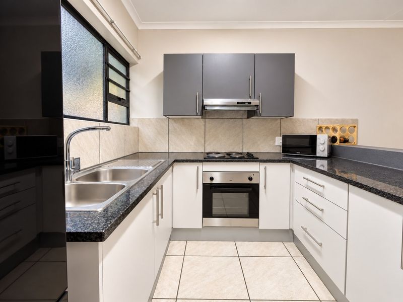 Modern kitchen featuring granite countertops, built-in oven, electric hob, extractor fan, and ample storage cabinetry with a double bowl stainless steel sink.