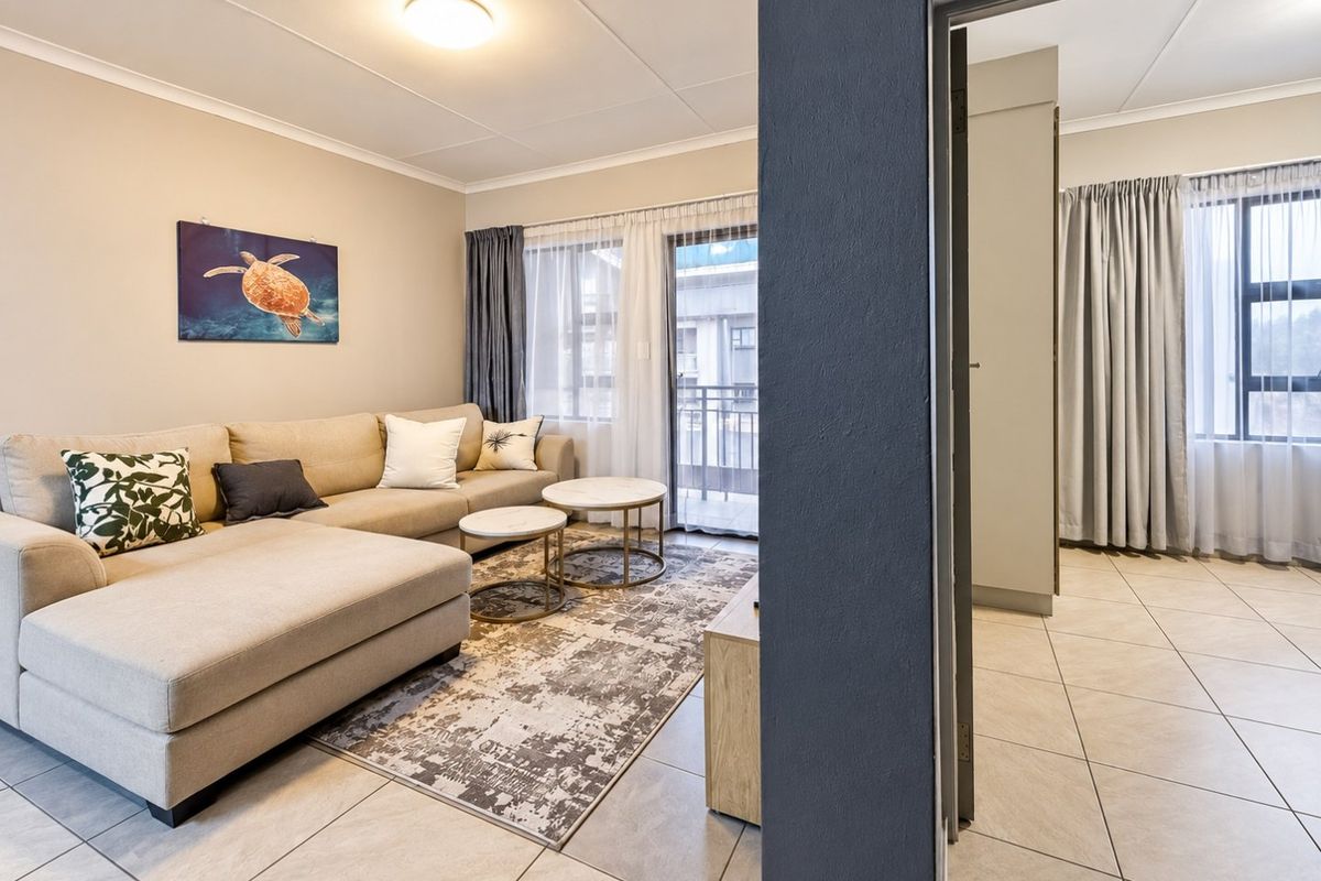 A well-maintained living area featuring neutral tiled flooring, a sliding glass door leading to a balcony, and adjacent built-in storage.