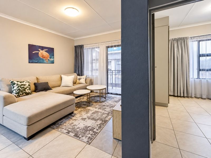 A well-maintained living area featuring neutral tiled flooring, a sliding glass door leading to a balcony, and adjacent built-in storage.
