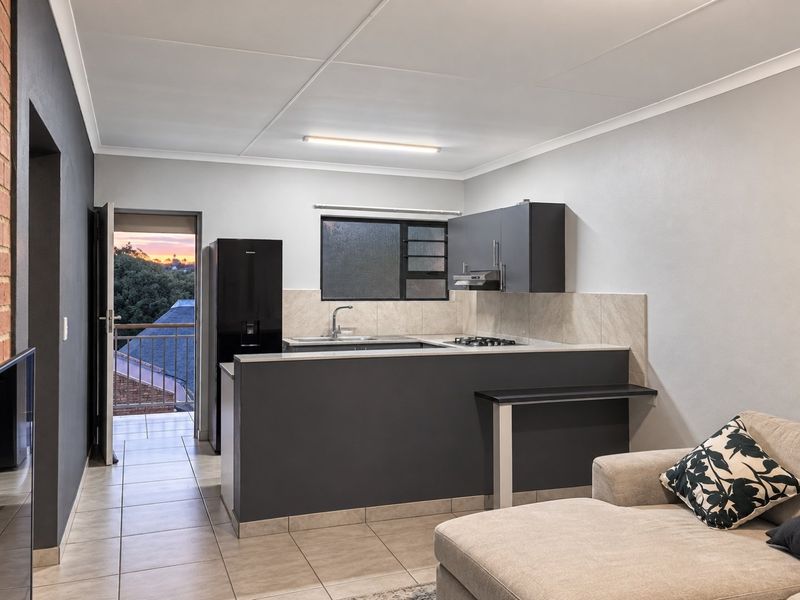 Open-plan kitchen and living area featuring modern dark cabinetry, a gas hob, tiled flooring, and direct access to a balcony.