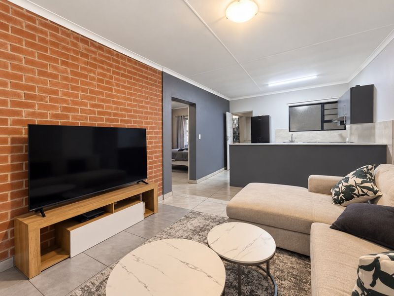 Open plan living area featuring an exposed brick wall, tiled flooring, and a functional kitchen space with modern cabinetry.