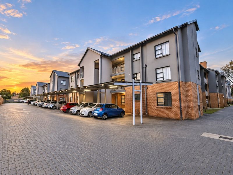 A modern apartment complex exterior featuring a paved driveway, covered parking bays, and a combination of brick and rendered facade finishes.