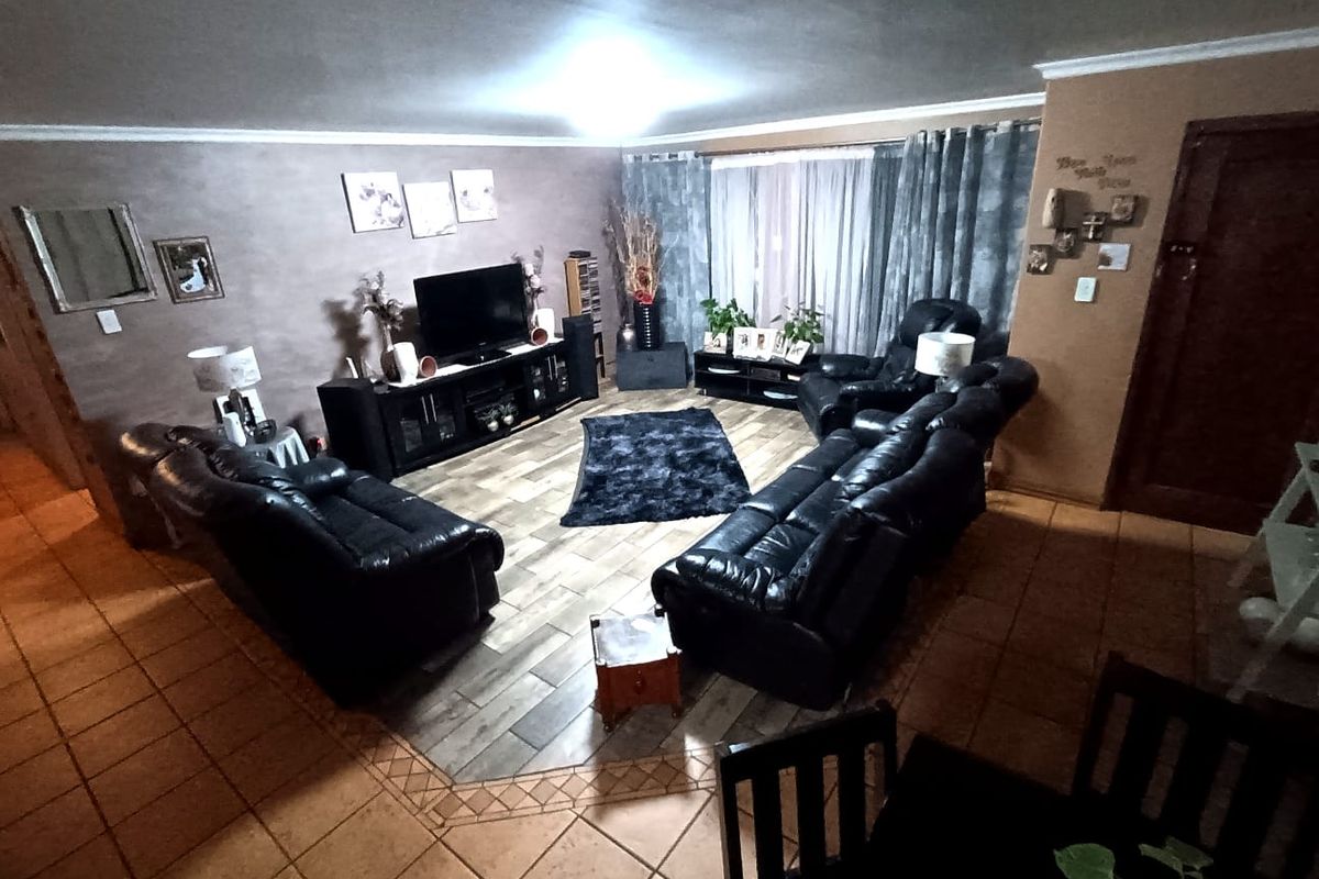 A spacious living room featuring a combination of traditional ceramic tiles and a central wood-look tile inlay, creating a defined seating area.
