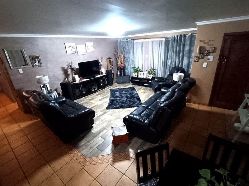 A spacious living room featuring a combination of traditional ceramic tiles and a central wood-look tile inlay, creating a defined seating area.