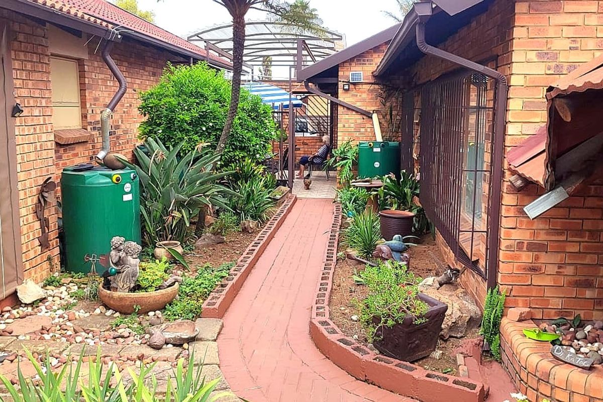 A narrow rear courtyard featuring brick paving, established garden beds, and functional rainwater collection tanks between two brick building wings.