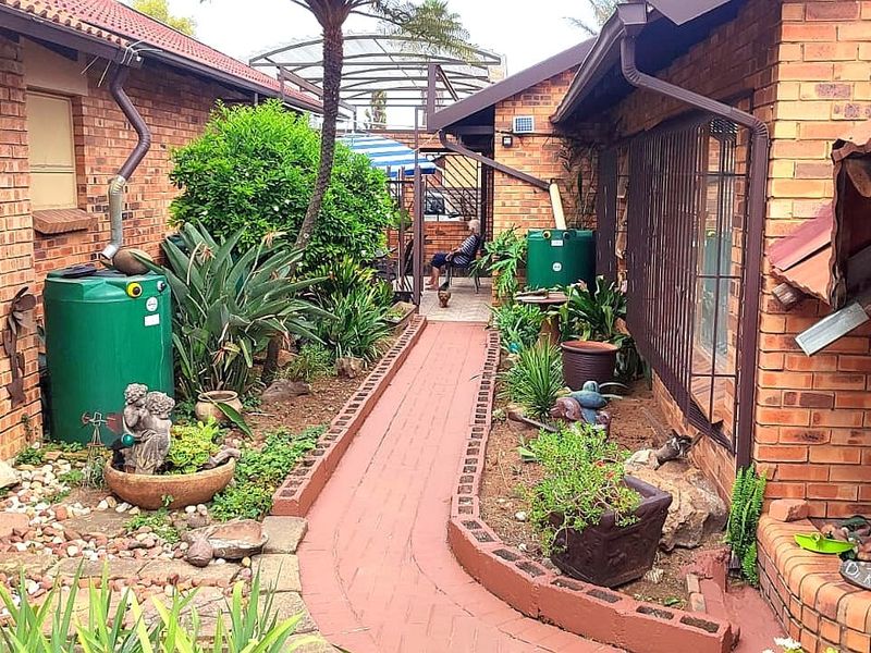 A narrow rear courtyard featuring brick paving, established garden beds, and functional rainwater collection tanks between two brick building wings.