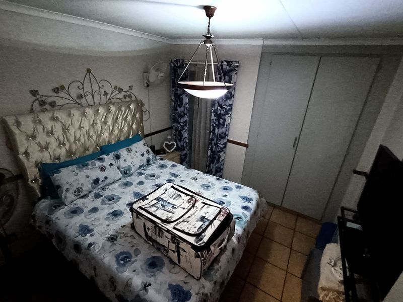 A bedroom featuring built-in cupboards, tiled flooring, and a central pendant light fixture.