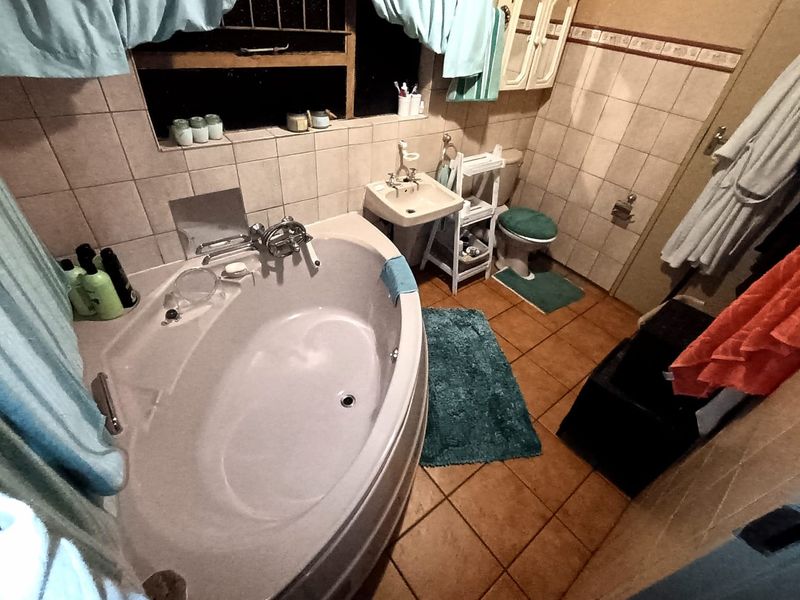 A functional bathroom featuring a corner bathtub, wall-mounted basin, and toilet with dated ceramic tile finishes throughout.