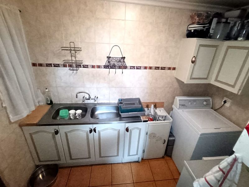 A functional laundry area featuring a double stainless steel sink, tiled splashback, and built-in cabinetry with space for a washing machine.