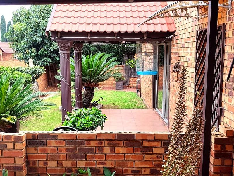 A covered patio area featuring tiled flooring and decorative columns, providing access to the garden through sliding glass doors.