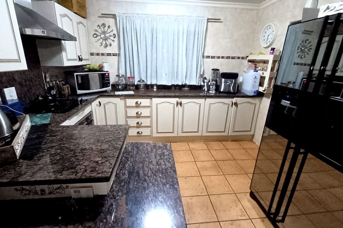 A functional kitchen featuring granite countertops, ample built-in cabinetry, a tiled backsplash, and ceramic floor tiles.