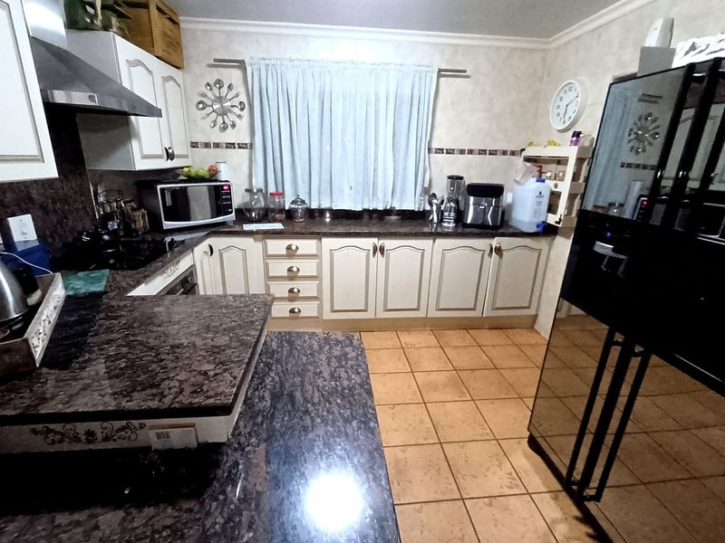 A functional kitchen featuring granite countertops, ample built-in cabinetry, a tiled backsplash, and ceramic floor tiles.