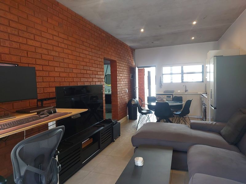 Open-plan living area featuring an exposed brick feature wall, tiled flooring, recessed lighting, and an integrated kitchen space.
