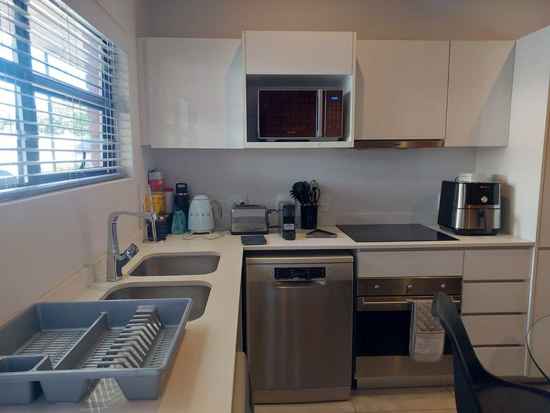 Modern kitchen featuring white cabinetry, stainless steel appliances including a built-in oven, hob, and dishwasher, with a double sink and window blinds.