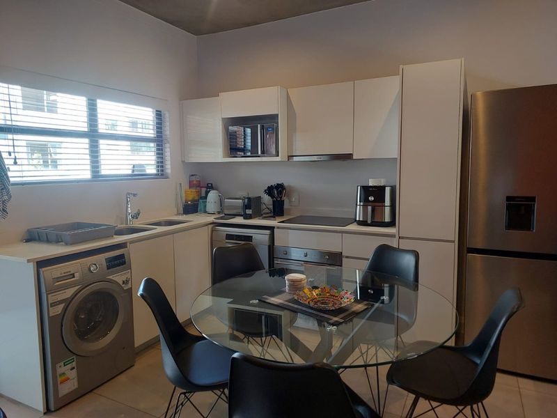 Modern open-plan kitchen featuring sleek white cabinetry, integrated appliances, stainless steel finishes, and tiled flooring, seamlessly connected to a dining area.
