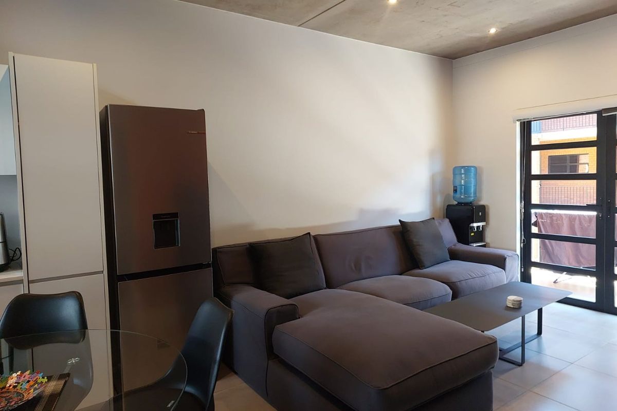 Open plan living area featuring modern tiled flooring, an exposed concrete ceiling with recessed lighting, and direct access to an outdoor balcony.