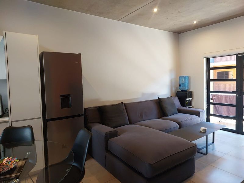 Open plan living area featuring modern tiled flooring, an exposed concrete ceiling with recessed lighting, and direct access to an outdoor balcony.