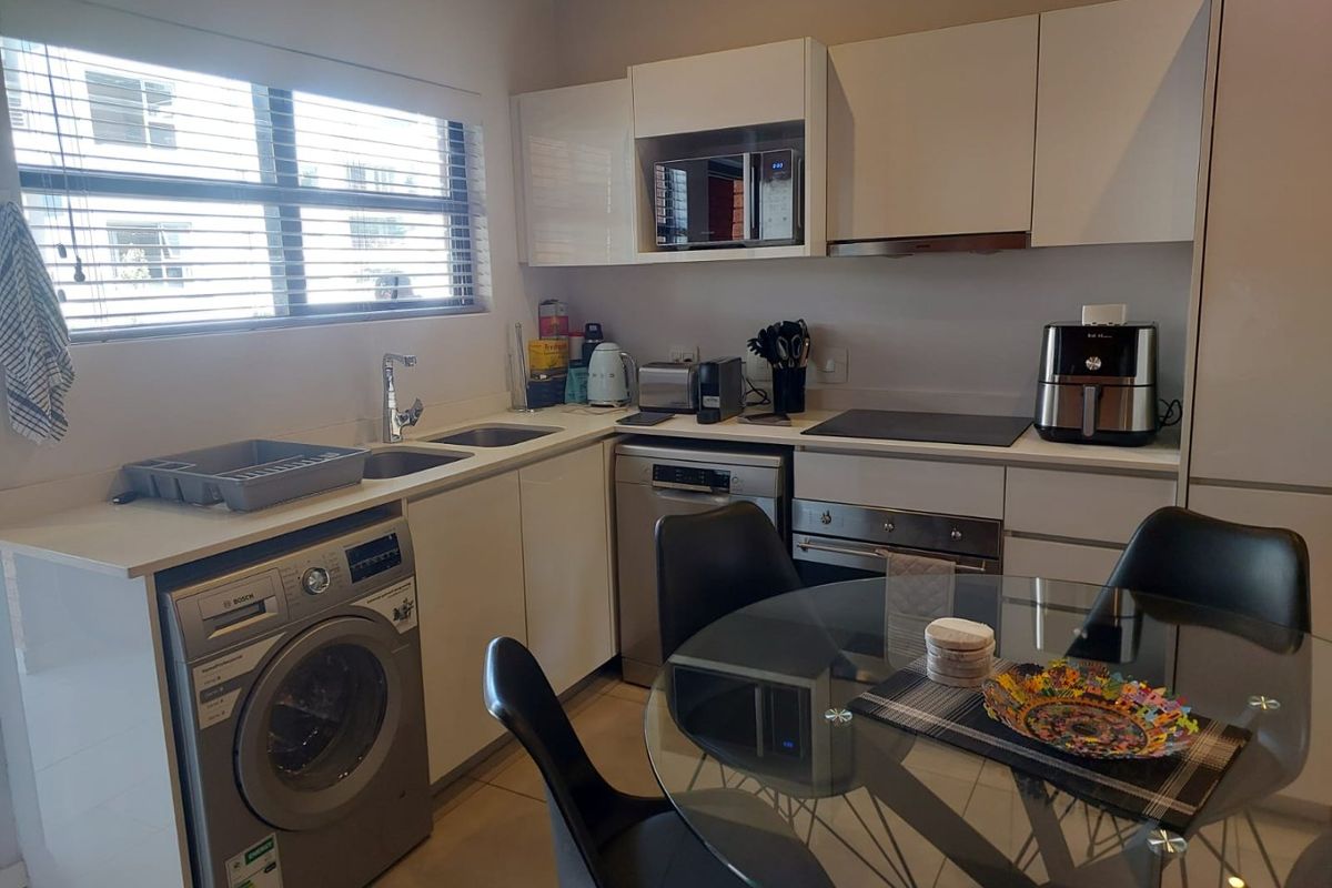 Modern kitchen featuring white cabinetry, integrated appliances including an oven, hob, and dishwasher, with a stainless steel sink and venetian blinds.