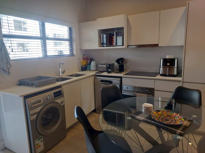 Modern kitchen featuring white cabinetry, integrated appliances including an oven, hob, and dishwasher, with a stainless steel sink and venetian blinds.