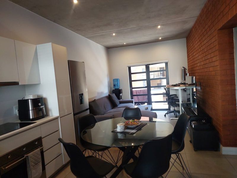 Modern open-plan living area featuring a sleek kitchen with built-in appliances, an exposed brick feature wall, and direct access to a balcony.