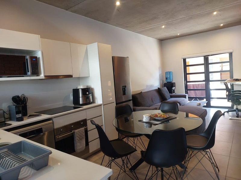 Modern open-plan living area featuring a sleek kitchen with built-in appliances, exposed concrete ceilings, and direct access to an outdoor space.