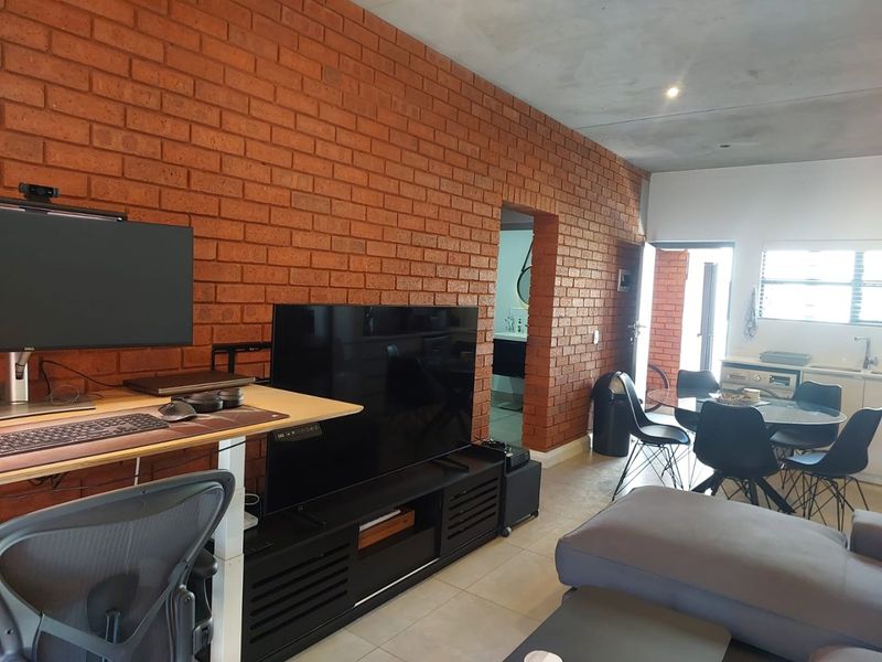 Open-plan living area featuring an exposed brick feature wall, tiled flooring, and integrated kitchen space with modern finishes.