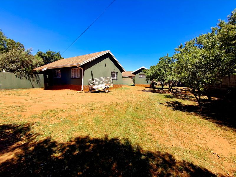 Rear view of the property featuring a large garden area with established trees, perimeter walling, and a tiled roof structure.