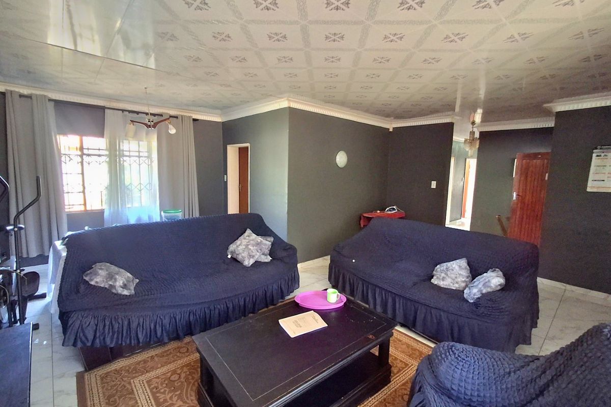 A living room featuring tiled flooring, patterned ceiling tiles, and security bars on the windows, offering a functional space with potential for modernization.