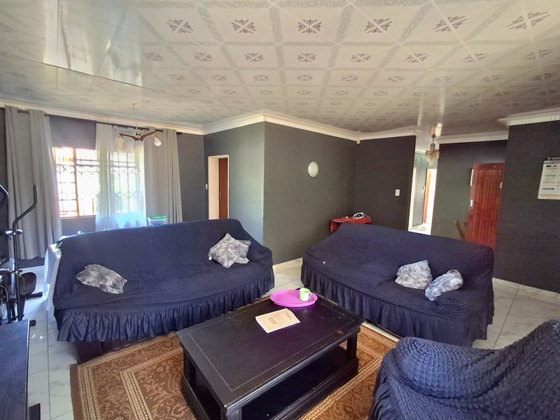 A living room featuring tiled flooring, patterned ceiling tiles, and security bars on the windows, offering a functional space with potential for modernization.