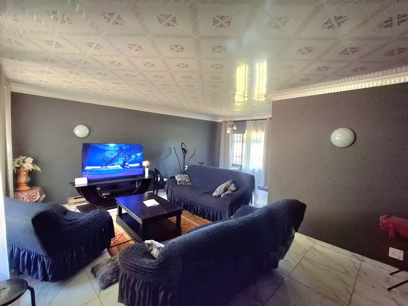 A living room featuring tiled flooring, decorative ceiling panels, and wall-mounted lighting, providing a functional space for relaxation.