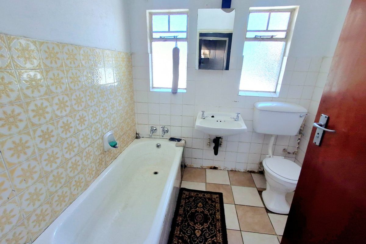 A dated bathroom featuring a bathtub, wall-mounted basin, and toilet with original tiled finishes, requiring modernization and repair of floor and wall surfaces.