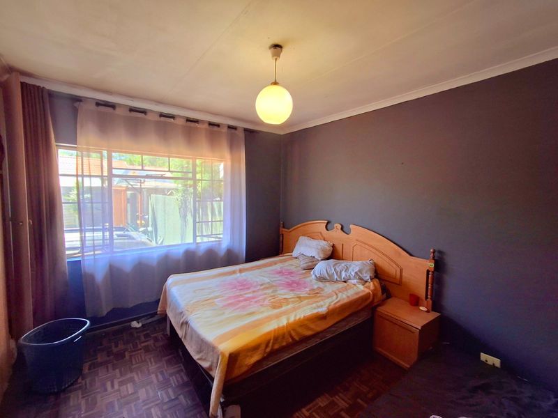 A bedroom featuring parquet flooring, a large window, and dark accent walls, requiring some ceiling maintenance and cosmetic updates.