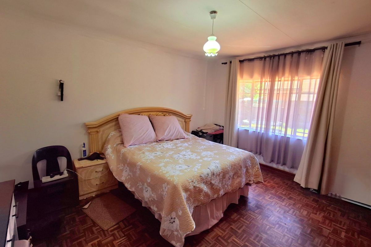 A bedroom featuring classic parquet flooring, neutral walls, and a large window with installed curtain rails, providing a functional and well-lit living space.
