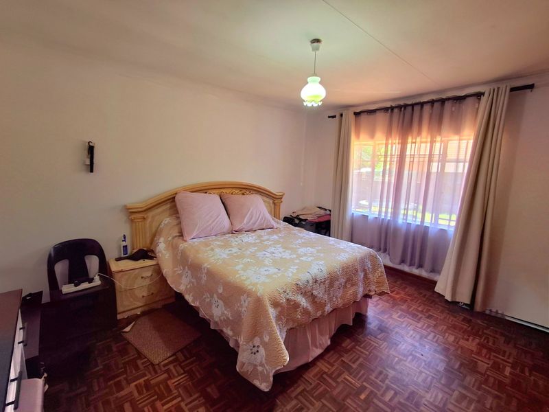 A bedroom featuring classic parquet flooring, neutral walls, and a large window with installed curtain rails, providing a functional and well-lit living space.