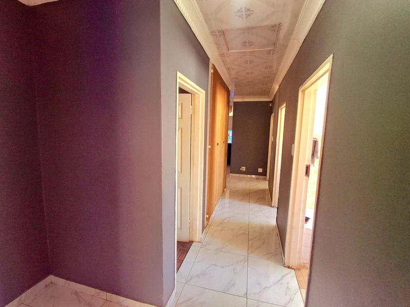 A functional hallway featuring marble-look tiled flooring, built-in storage cupboards, and decorative ceiling cornices connecting various rooms within the home.