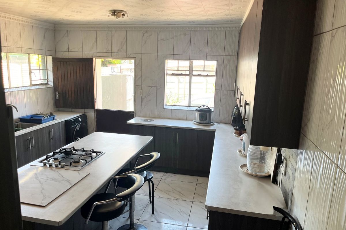 Modern kitchen featuring dark cabinetry, a central island with a gas hob, tiled finishes, and direct access to the exterior.