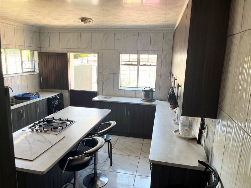 Modern kitchen featuring dark cabinetry, a central island with a gas hob, tiled finishes, and direct access to the exterior.
