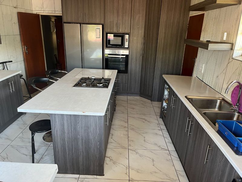 Modern kitchen featuring dark wood-grain cabinetry, a central island with a gas hob, stone countertops, and integrated appliances.