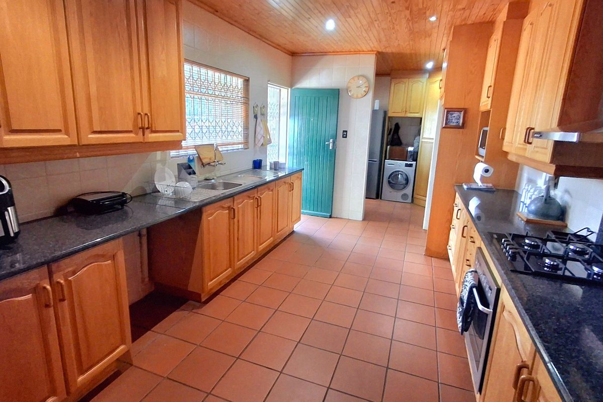 Spacious kitchen featuring warm wooden cabinetry, granite countertops, integrated appliances, and tiled flooring, with an adjacent laundry area and direct exterior access.