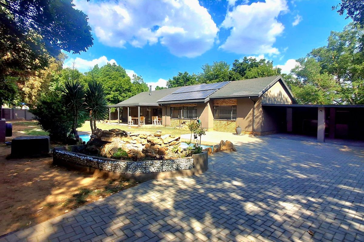 Spacious rear exterior featuring a paved driveway, covered patio, swimming pool, and solar panels installed on the roof.