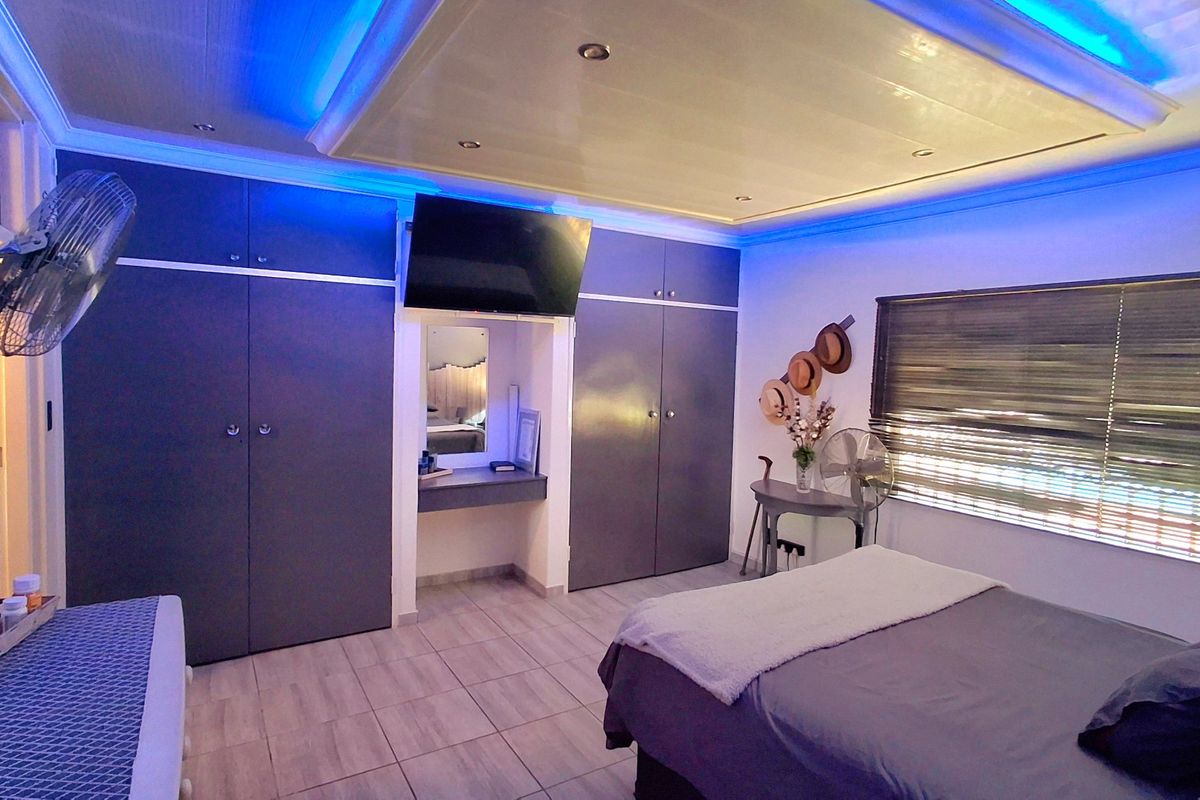 A well-maintained bedroom featuring extensive built-in cabinetry, a dedicated vanity area, tiled flooring, and modern recessed ceiling lighting with ambient blue accents.