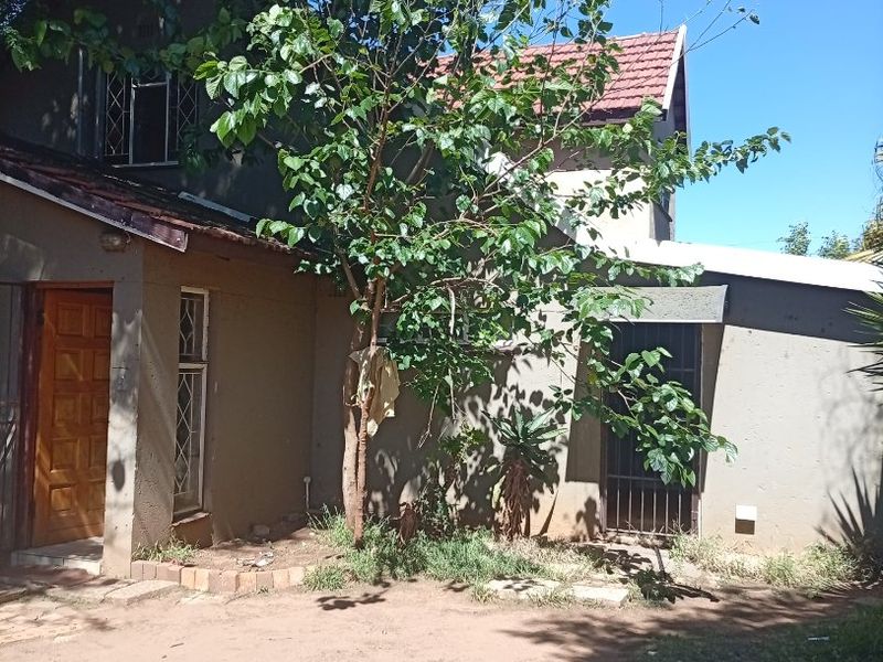 Front elevation of a two-story house featuring a tiled roof, timber entrance door, and security gate, set within a natural garden area.