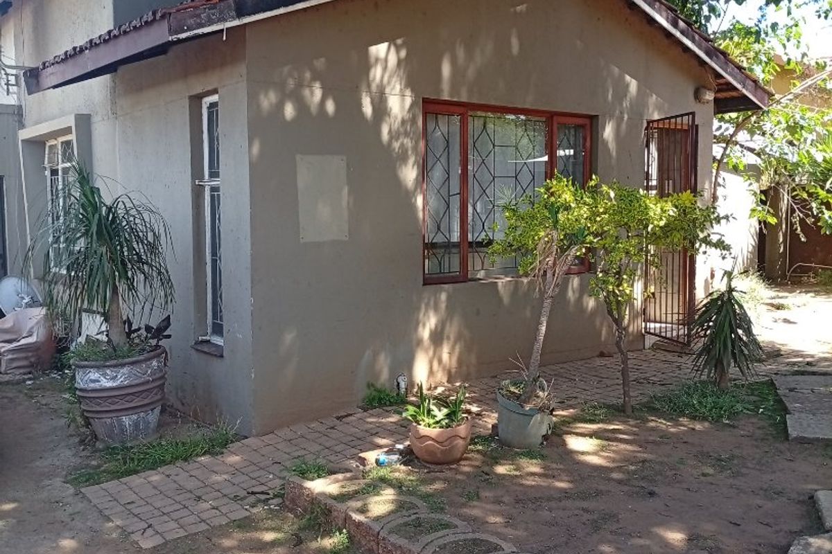 Rear view of a residential house featuring a tiled roof, security gate, and paved walkway with established garden surroundings.