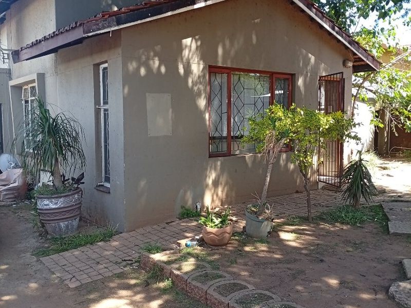 Rear view of a residential house featuring a tiled roof, security gate, and paved walkway with established garden surroundings.