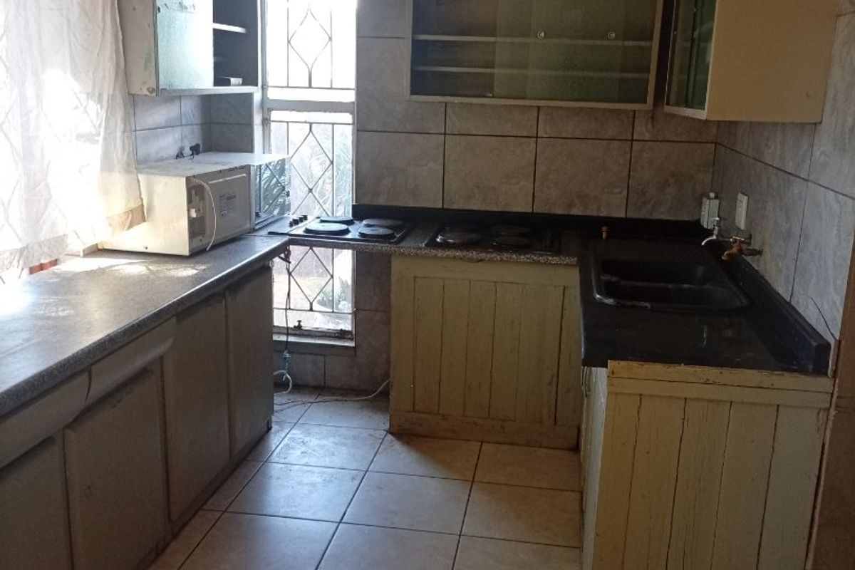 A dated kitchen featuring tiled walls and flooring, built-in cabinetry, and a built-in hob, requiring significant renovation to modernize the space.