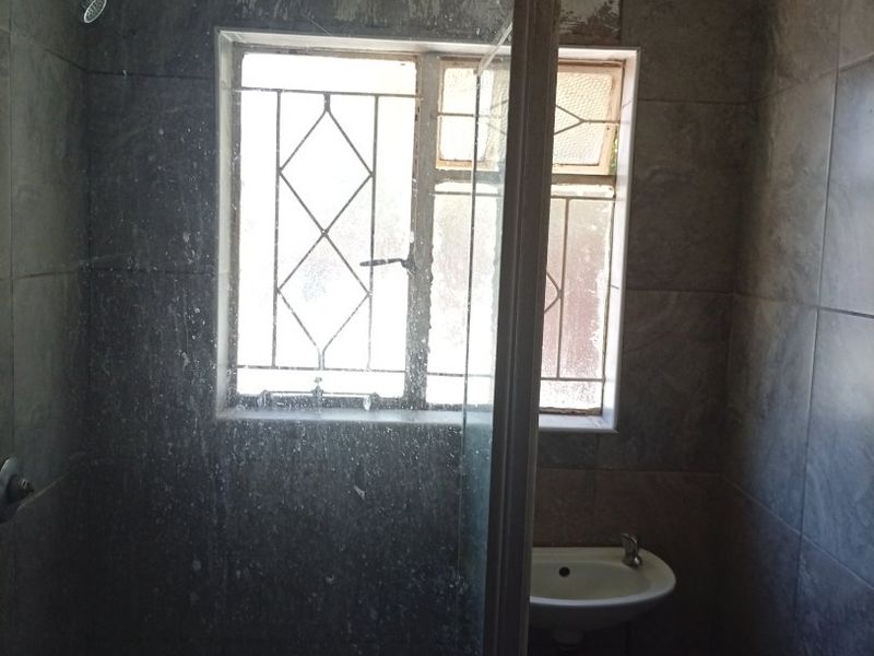 A small bathroom featuring a shower enclosure and wall-mounted basin, currently requiring renovation and repair to the wall finishes.